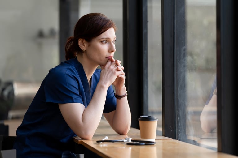 Tired female doctor or nurse with stethoscope looking out window, thinking in cafe.